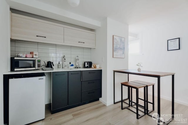 kitchen featuring gray cabinets, light wood-type flooring, decorative backsplash, sink, and fridge