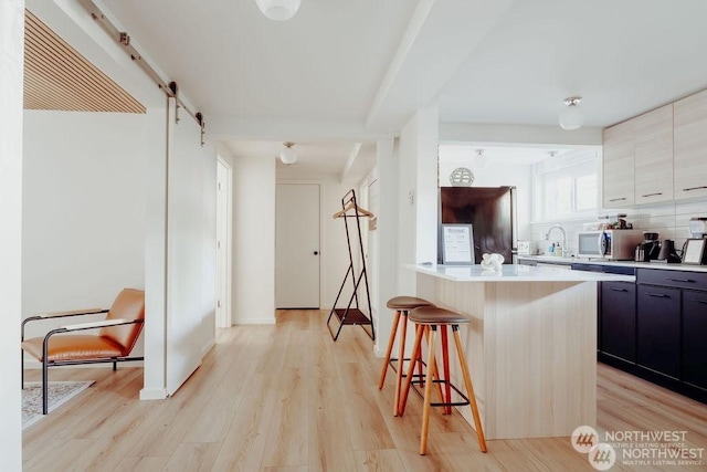 kitchen featuring a center island, light wood-type flooring, tasteful backsplash, a breakfast bar area, and a barn door