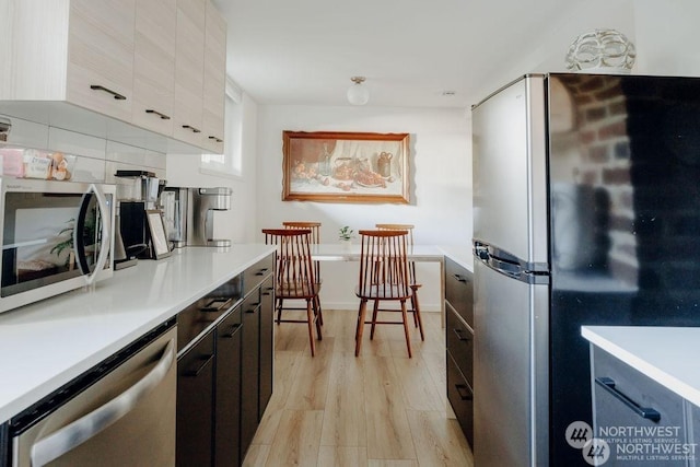 kitchen with appliances with stainless steel finishes, light hardwood / wood-style floors, white cabinets, and backsplash