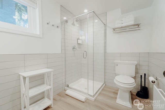 bathroom with tile walls, wood-type flooring, an enclosed shower, and toilet