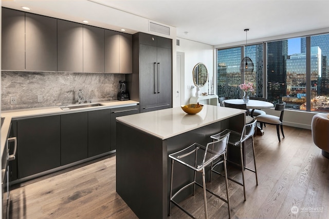 kitchen with sink, a center island, light hardwood / wood-style floors, decorative light fixtures, and a breakfast bar