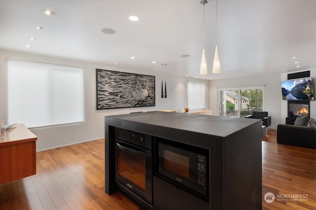 kitchen featuring pendant lighting, a kitchen island, black microwave, and light hardwood / wood-style flooring