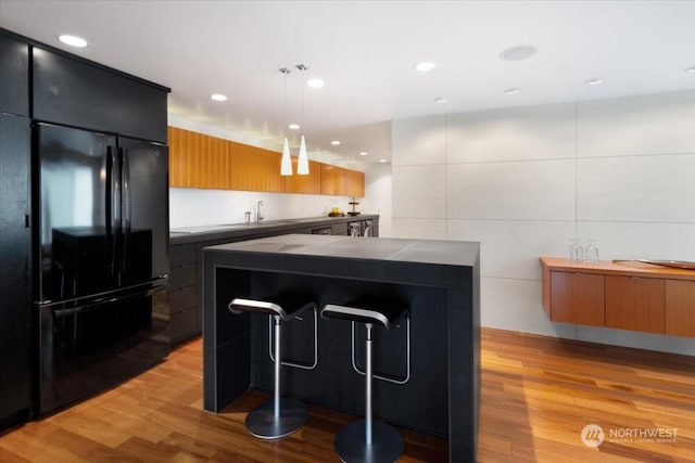 kitchen featuring light wood-type flooring, pendant lighting, a center island, and black fridge