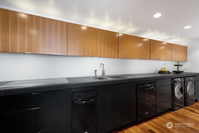 kitchen featuring sink, washing machine and dryer, light wood-type flooring, black dishwasher, and stovetop