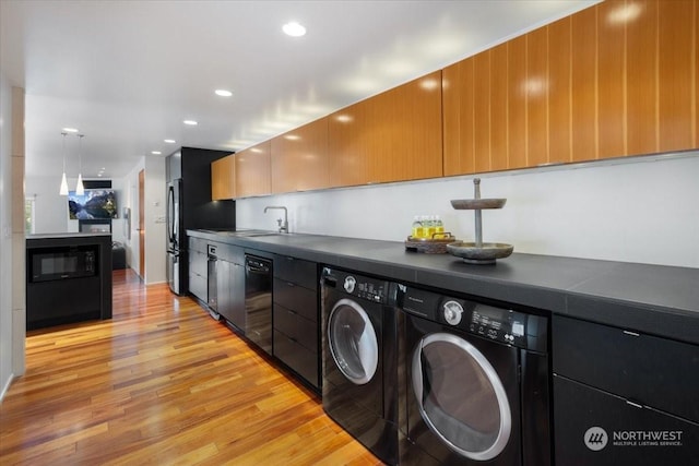 interior space featuring black appliances, sink, hanging light fixtures, independent washer and dryer, and light wood-type flooring