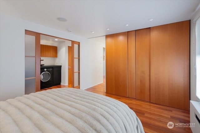 bedroom with washer / dryer, light wood-type flooring, and a closet