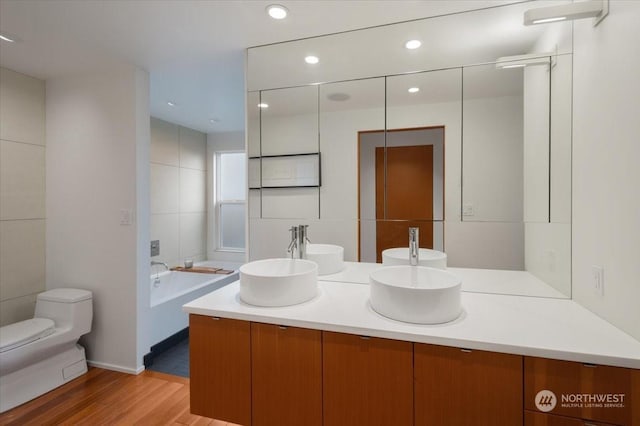 bathroom featuring a tub, hardwood / wood-style floors, toilet, vanity, and tile walls