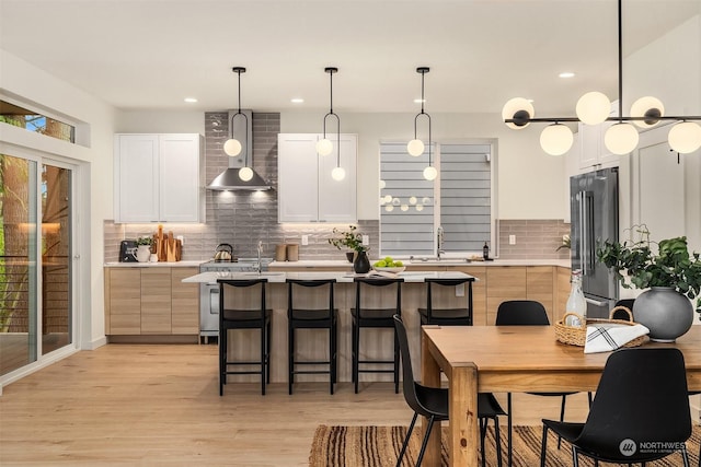 kitchen featuring wall chimney exhaust hood, decorative backsplash, appliances with stainless steel finishes, decorative light fixtures, and white cabinetry