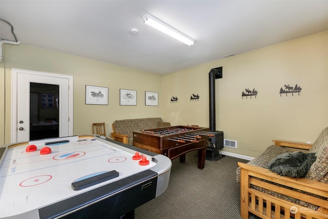 game room featuring a wood stove and dark colored carpet