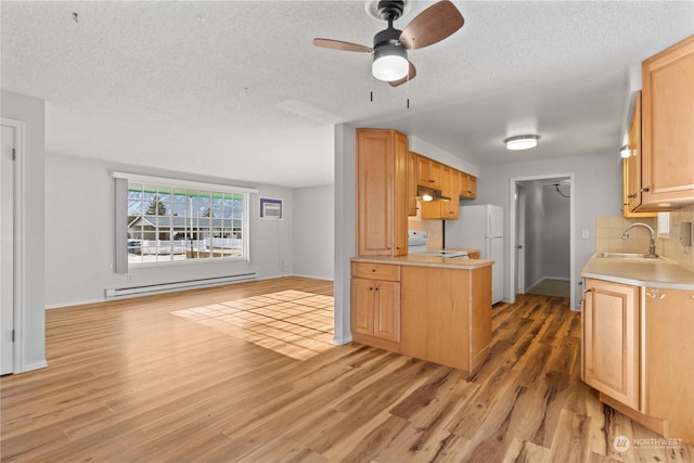 kitchen with sink, white refrigerator, a baseboard heating unit, decorative backsplash, and light wood-type flooring