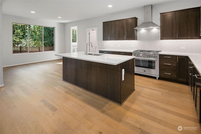 kitchen with sink, high end stainless steel range oven, wall chimney range hood, an island with sink, and decorative backsplash