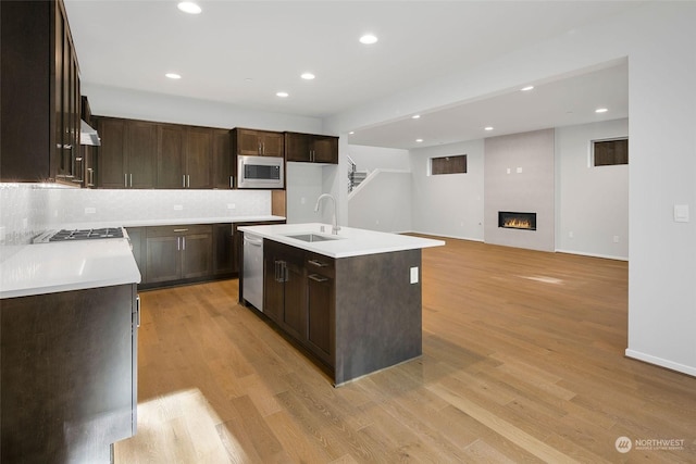 kitchen with sink, stainless steel appliances, backsplash, a fireplace, and a center island with sink