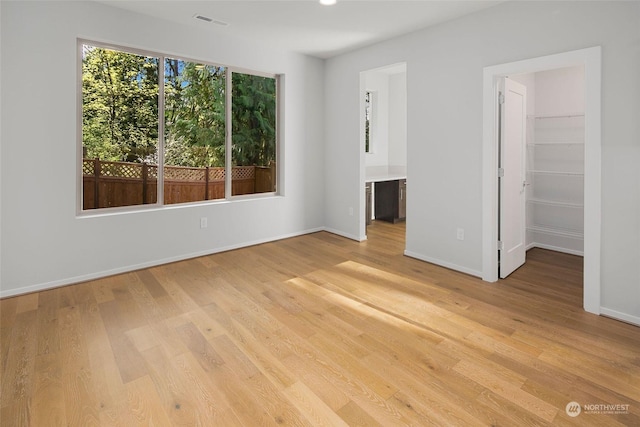 unfurnished bedroom with connected bathroom, a walk in closet, a closet, and light wood-type flooring