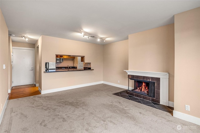 unfurnished living room featuring dark colored carpet, rail lighting, and a tiled fireplace