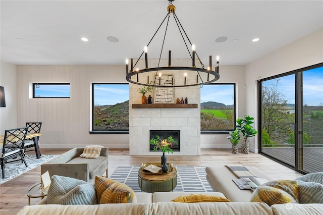 living room with a tiled fireplace, a healthy amount of sunlight, a notable chandelier, and light hardwood / wood-style floors