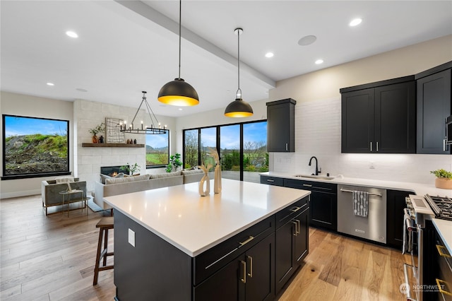 kitchen featuring stainless steel appliances, sink, pendant lighting, a fireplace, and a kitchen island