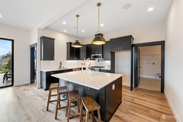 kitchen featuring a kitchen bar, light wood-type flooring, stainless steel appliances, a kitchen island, and hanging light fixtures