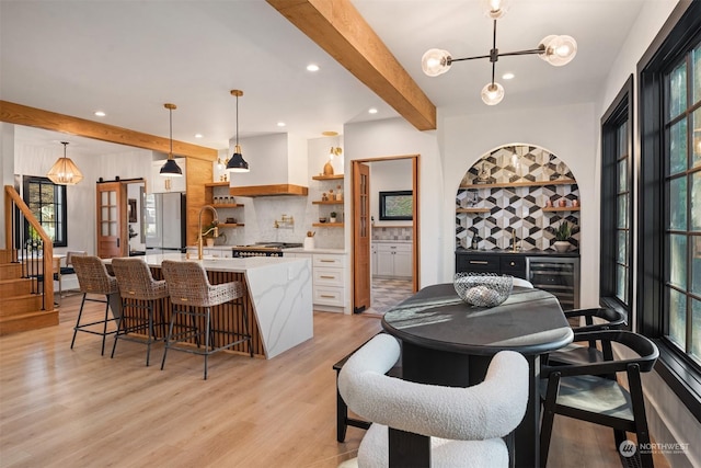 dining space with wine cooler, beam ceiling, light hardwood / wood-style flooring, an inviting chandelier, and sink