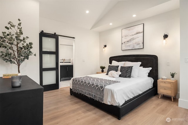 bedroom with light hardwood / wood-style flooring, connected bathroom, lofted ceiling, a barn door, and sink