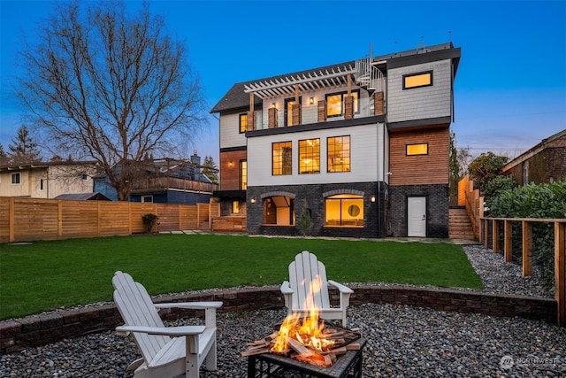 back house at dusk featuring a lawn, a fire pit, and a balcony