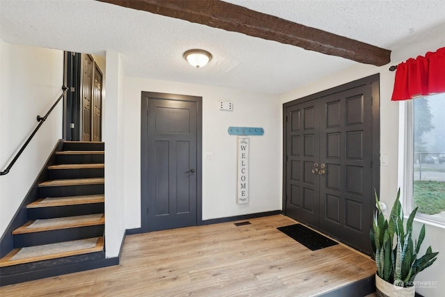 foyer entrance featuring a textured ceiling, light hardwood / wood-style flooring, and beamed ceiling