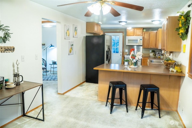 kitchen featuring light carpet, kitchen peninsula, white appliances, sink, and a breakfast bar area