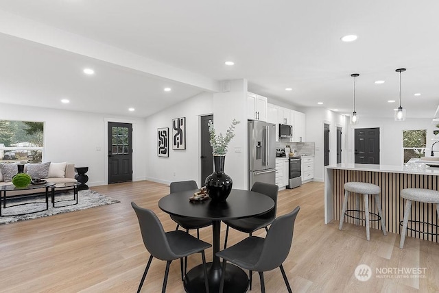 dining area with lofted ceiling with beams, sink, and light hardwood / wood-style flooring