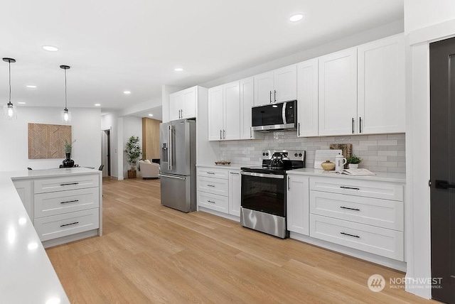 kitchen featuring white cabinets, pendant lighting, stainless steel appliances, and light hardwood / wood-style flooring