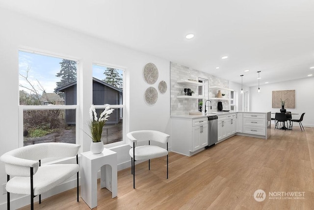 kitchen featuring white cabinetry, dishwasher, sink, light hardwood / wood-style floors, and decorative light fixtures