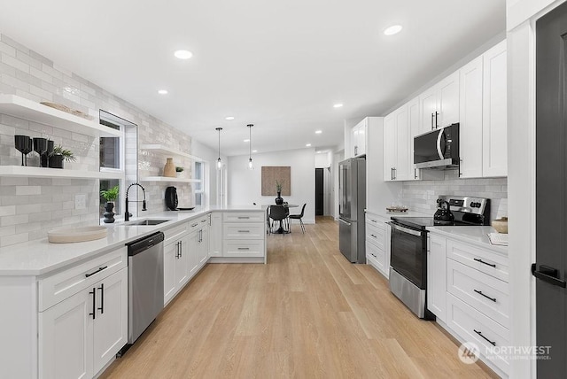 kitchen featuring kitchen peninsula, stainless steel appliances, sink, decorative light fixtures, and white cabinetry