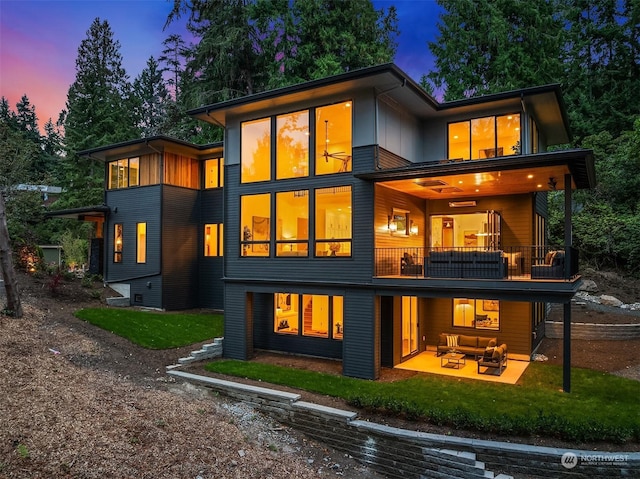 back house at dusk featuring a lawn, an outdoor living space, a balcony, and a patio