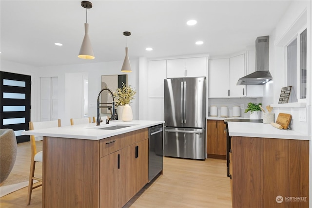 kitchen with white cabinetry, sink, wall chimney range hood, a center island with sink, and appliances with stainless steel finishes