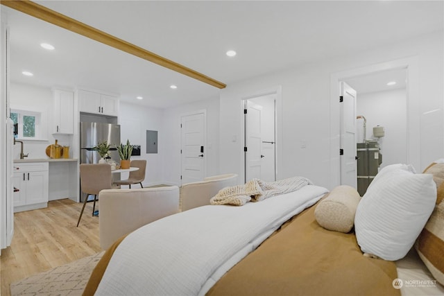 bedroom with electric panel, stainless steel fridge, light wood-type flooring, connected bathroom, and beamed ceiling