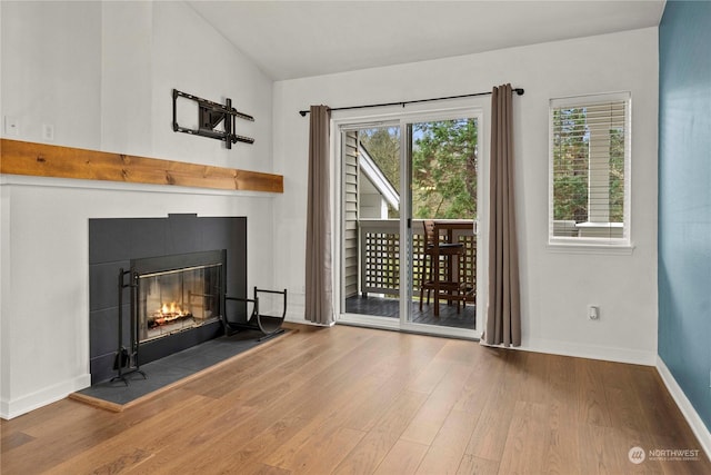 unfurnished living room featuring lofted ceiling, hardwood / wood-style flooring, and a tiled fireplace