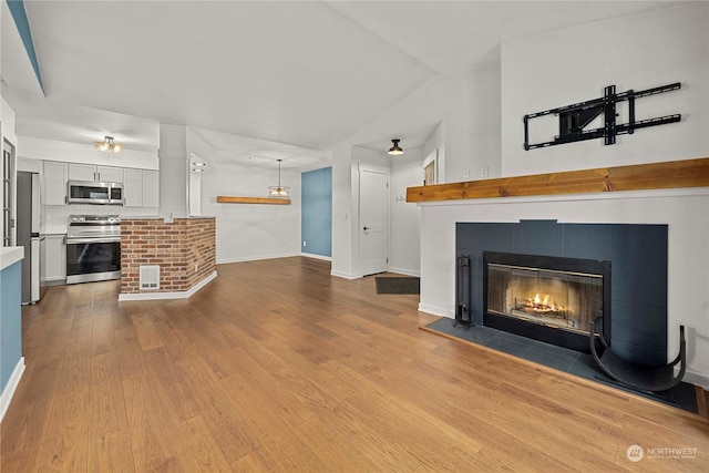 unfurnished living room featuring lofted ceiling, a tile fireplace, and light hardwood / wood-style flooring