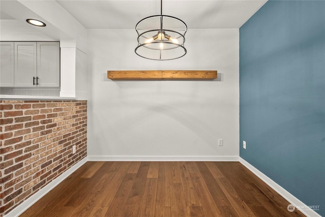 unfurnished dining area with dark wood-type flooring and brick wall