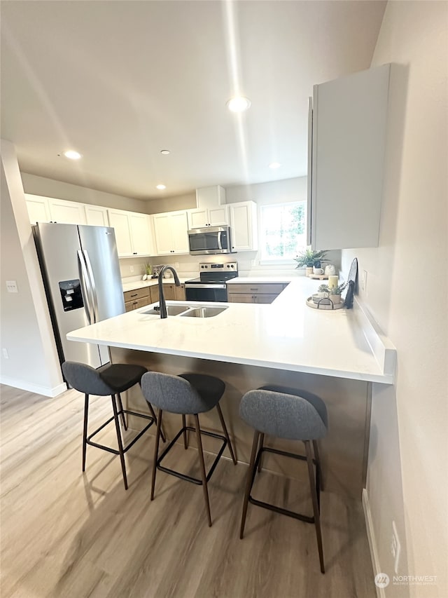 kitchen featuring stainless steel appliances, white cabinetry, sink, and a breakfast bar area