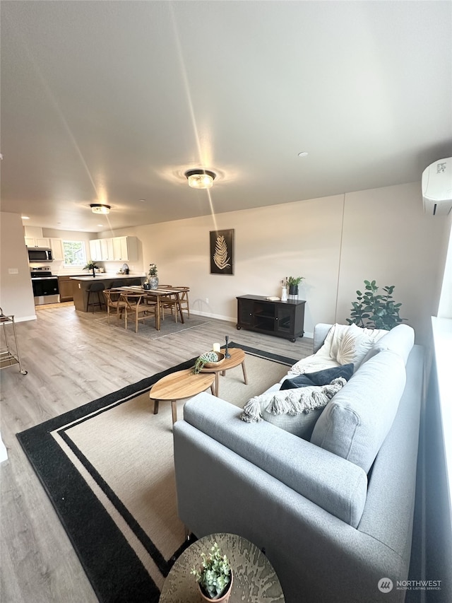 living room with a wall mounted AC and light hardwood / wood-style flooring