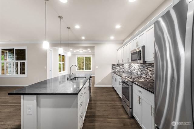 kitchen with appliances with stainless steel finishes, sink, pendant lighting, white cabinetry, and an island with sink