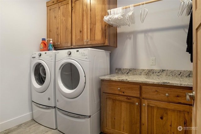 clothes washing area with washing machine and dryer, light wood-type flooring, and cabinets