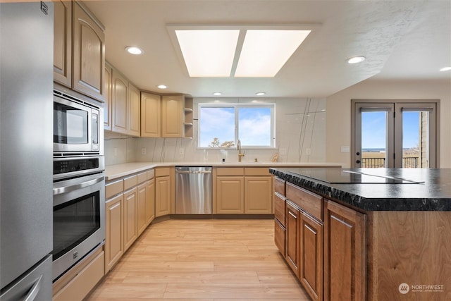 kitchen featuring sink, tasteful backsplash, light wood-type flooring, light brown cabinetry, and appliances with stainless steel finishes