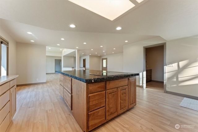 kitchen featuring black electric stovetop, light hardwood / wood-style floors, a kitchen island, and dark stone countertops