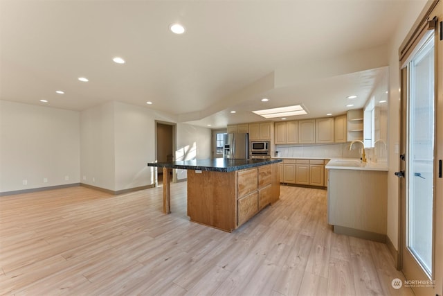 kitchen featuring light brown cabinets, stainless steel appliances, light hardwood / wood-style floors, a breakfast bar area, and a kitchen island