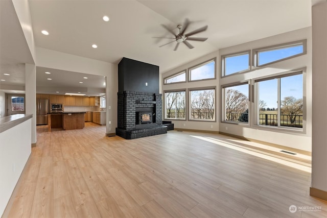 unfurnished living room featuring a brick fireplace, light hardwood / wood-style floors, vaulted ceiling, and ceiling fan