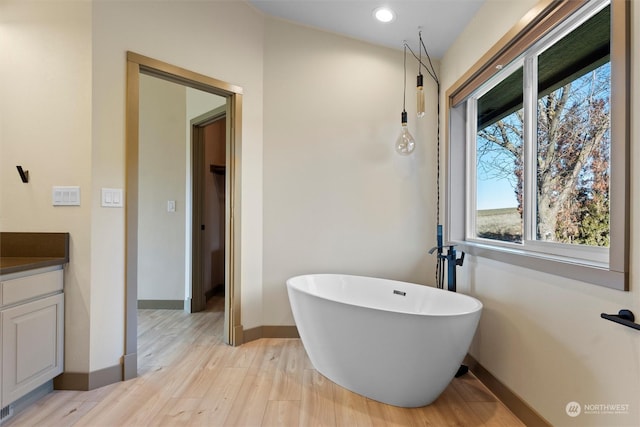 bathroom featuring hardwood / wood-style flooring, vanity, and a tub to relax in