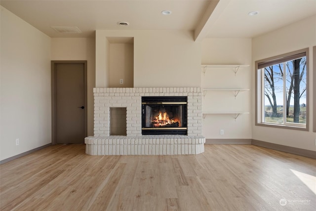 unfurnished living room featuring beam ceiling, a fireplace, and light hardwood / wood-style flooring