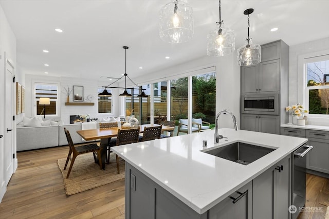 kitchen featuring pendant lighting, a center island with sink, sink, gray cabinets, and light wood-type flooring