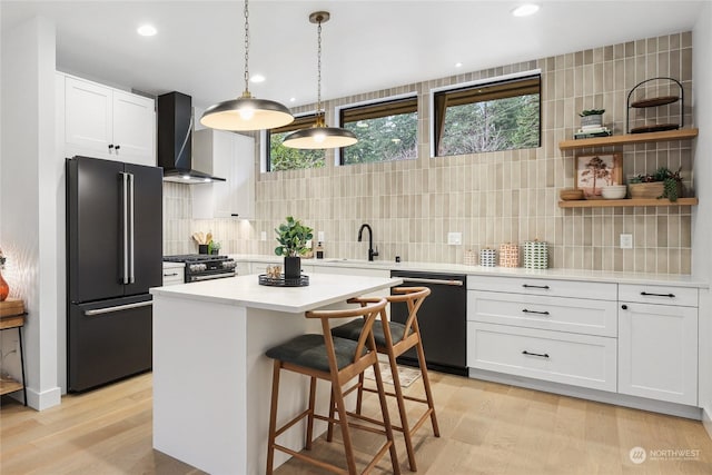 kitchen with high quality appliances, decorative backsplash, white cabinetry, and wall chimney exhaust hood