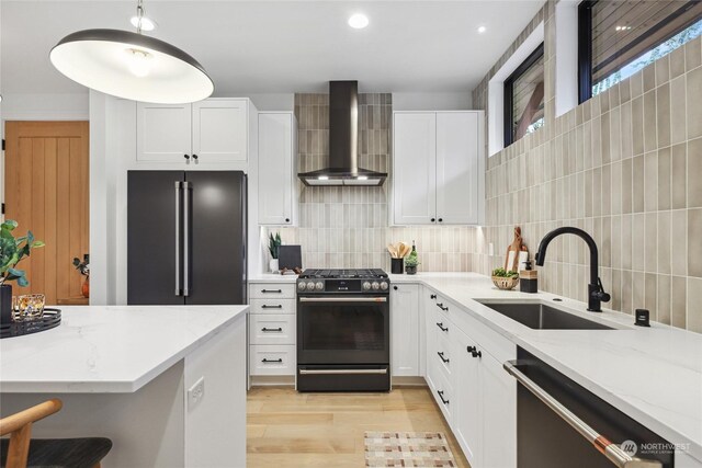 kitchen featuring wall chimney range hood, sink, decorative backsplash, white cabinetry, and stainless steel appliances