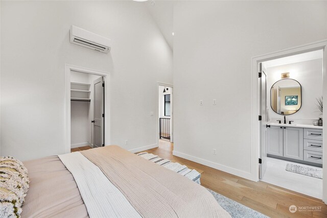 bedroom featuring ensuite bath, a spacious closet, light wood-type flooring, a towering ceiling, and a wall unit AC